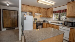 A kitchen with wooden cabinets, a granite countertop, a refrigerator, a stove, a microwave, and a window with a view of the outdoors.