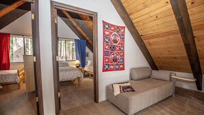 A cozy attic bedroom with a loft bed, a sofa, and a quilted tapestry on the wall.
