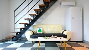 A modern living room with a checkered floor, a sofa, a coffee table, a framed picture, a staircase, and a white refrigerator. - Gyeongju The one Pension - Blue (Gyeongju)