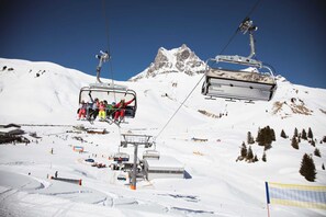 Un télésiège avec des passagers, un téléski, et une montagne enneigée en arrière-plan.