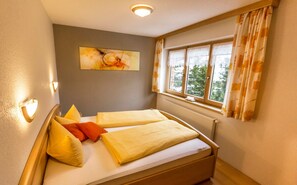A room with two beds, a window with curtains, a radiator, and a painting on the wall. - Top 3 - House Annette (Schröcken)