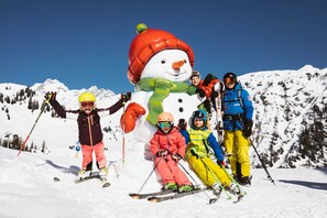 Un groupe de personnes fait du ski sur une montagne enneigée, et on peut voir un grand bonhomme de neige en guise de décoration.