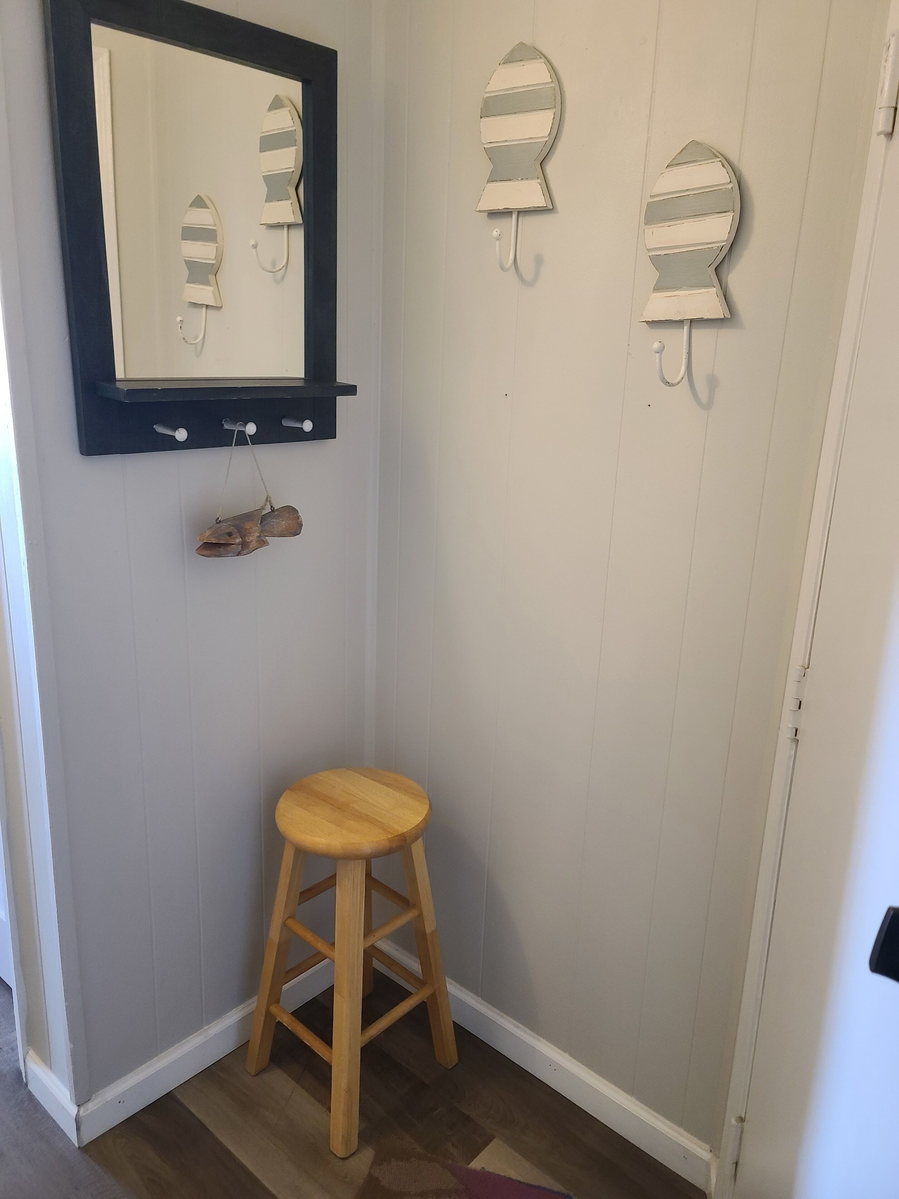 Un baño pequeño con un taburete de madera, un espejo y tres toalleros.