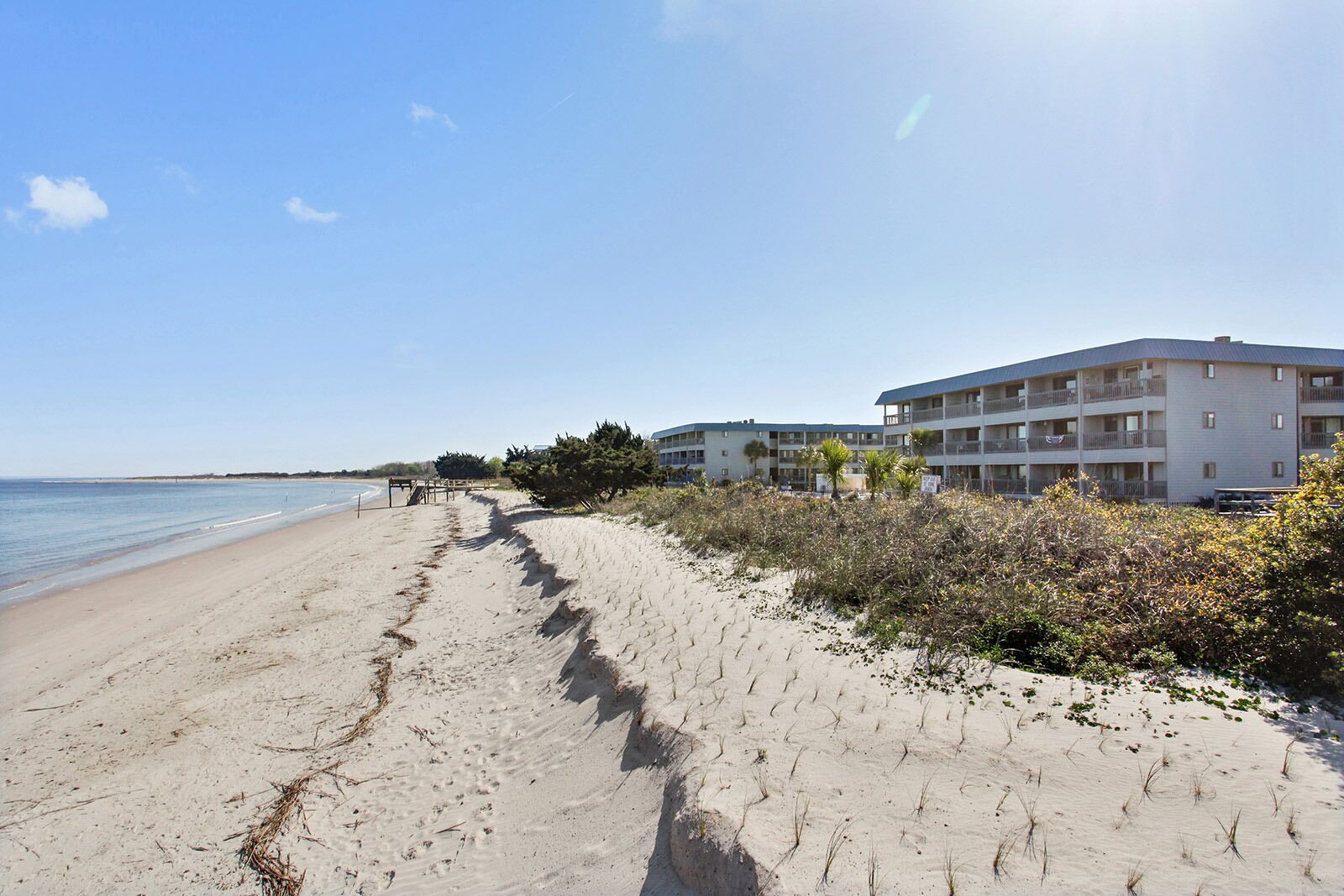 A beach with a sandy path leading to a building with multiple balconies.