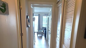 Un pasillo estrecho con suelo de madera y paredes blancas. Hay puertas a ambos lados y una ventana al final.