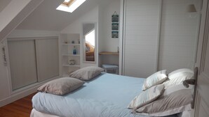 Ein Schlafzimmer mit Dachfenster, einem Bett mit vielen Kissen, einem weißen Kleiderschrank und einem kleinen Schreibtisch mit Stuhl.