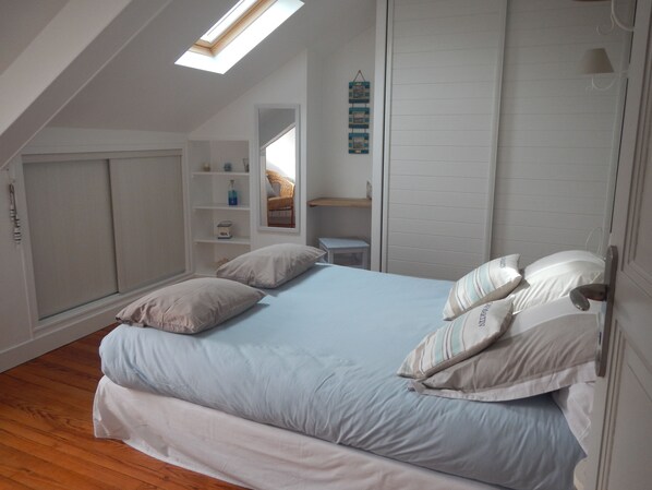 A bedroom with a skylight, a bed with multiple pillows, a white wardrobe, and a small desk with a chair. - Comfortable house overlooking the port and close to shops. (Port-En-Bessin-Huppain)