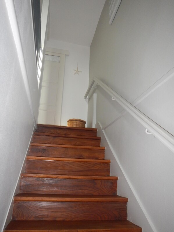Una escalera de madera con paredes blancas y un ventilador de techo.