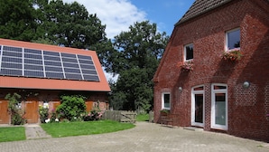Una casa de ladrillo con techo rojo, un camino de entrada pavimentado y un panel solar a la izquierda.
