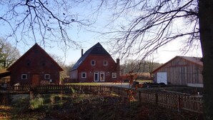 Entorno rural con una casa grande de ladrillo, un edificio más pequeño adyacente y un granero de madera.