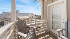 En træterrasse med en hvid stol og en glasdør, med udsigt over et boligområde med lignende huse.