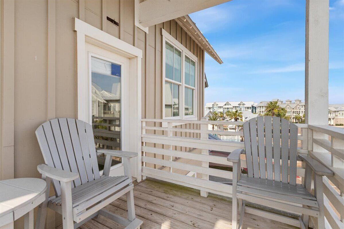 Una terraza de madera con dos sillas Adirondack y una mesa, con vista a una hilera de casas.