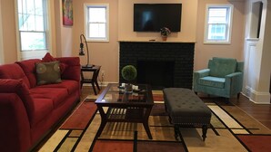 A living room with a red couch, a blue armchair, a black fireplace, and a flat-screen TV mounted above the fireplace. - Newly updated house close to the Clinic,UH, Case in Cleveland Hts. (Cleveland Heights)