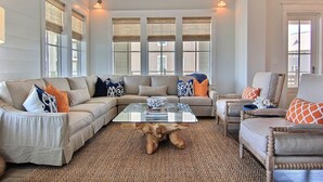 A living room with a sectional sofa, a glass coffee table, and a woven rug.