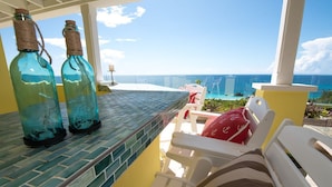 Un balcón con dos botellas, vista al océano y una zona de piscina.