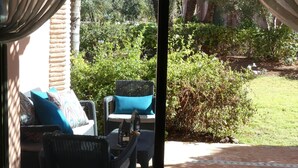 A view through a window with curtains, revealing an outdoor seating area with wicker furniture and a lawn. - A haven of peace in the heart of the palm grove (Marrakech)