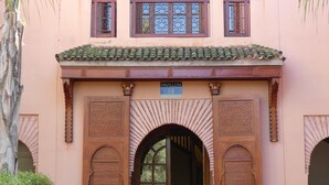 A building with a traditional architectural style, featuring a central entrance with two large wooden doors, a balcony with decorative railings, and a tiled roof. - A haven of peace in the heart of the palm grove (Marrakech)