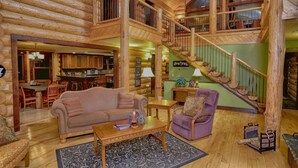 Interior espacioso de una cabaña de troncos, con sala de estar, comedor y una escalera que conduce a un nivel superior.