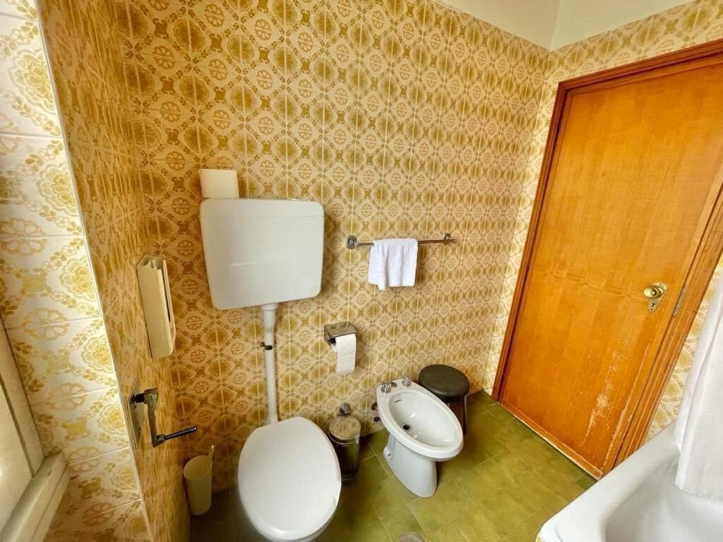 Casa de banho com sanita, bidé e porta de madeira.
