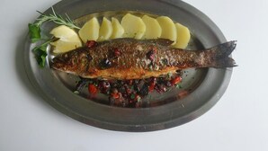 A whole grilled fish with lemon slices and herbs on a plate. - Hotel La Sorgente (Plesio)