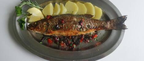 A whole grilled fish with lemon slices and herbs on a plate.