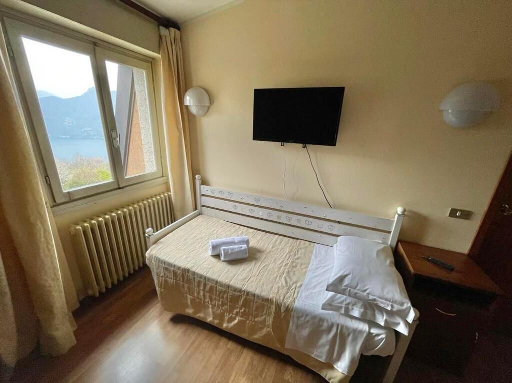 Ett hotellrum med en säng, en tv som är monterad på väggen och ett fönster med gardiner.