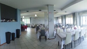 A spacious dining area with multiple tables and chairs, a wine rack on the left, and large windows allowing natural light. - Hotel La Sorgente (Plesio)
