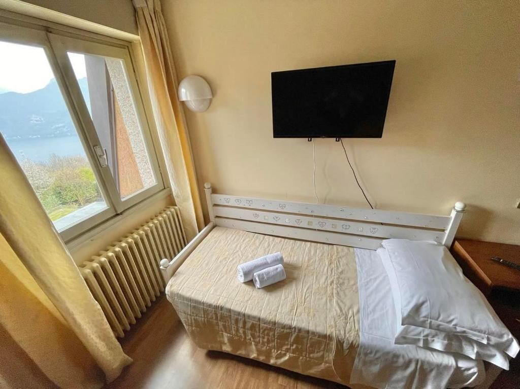 Une chambre d’hôtel avec un lit, un téléviseur fixé au mur, une fenêtre donnant sur un paysage agréable et un radiateur.