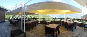 An outdoor dining area with tables and chairs under a large canopy, overlooking a mountainous landscape. - Hotel La Sorgente (Plesio)