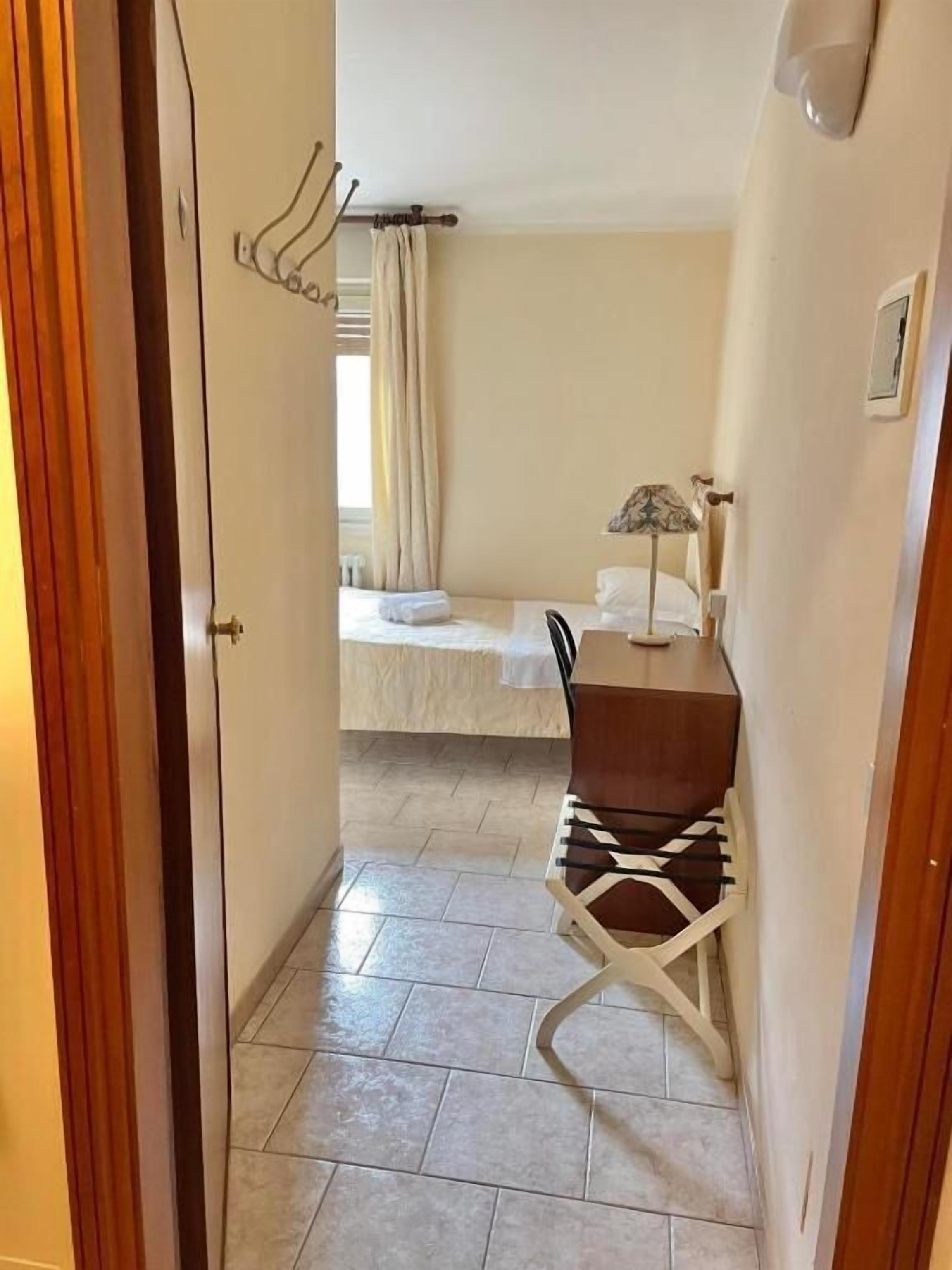 Un pasillo estrecho que conduce a un dormitorio con cama, escritorio con lámpara y silla.