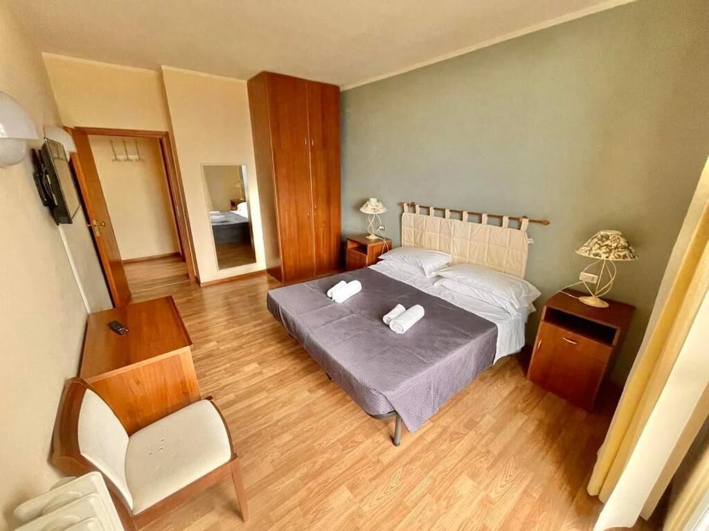 Un dormitorio con cama, mesitas de noche, una silla y un armario.