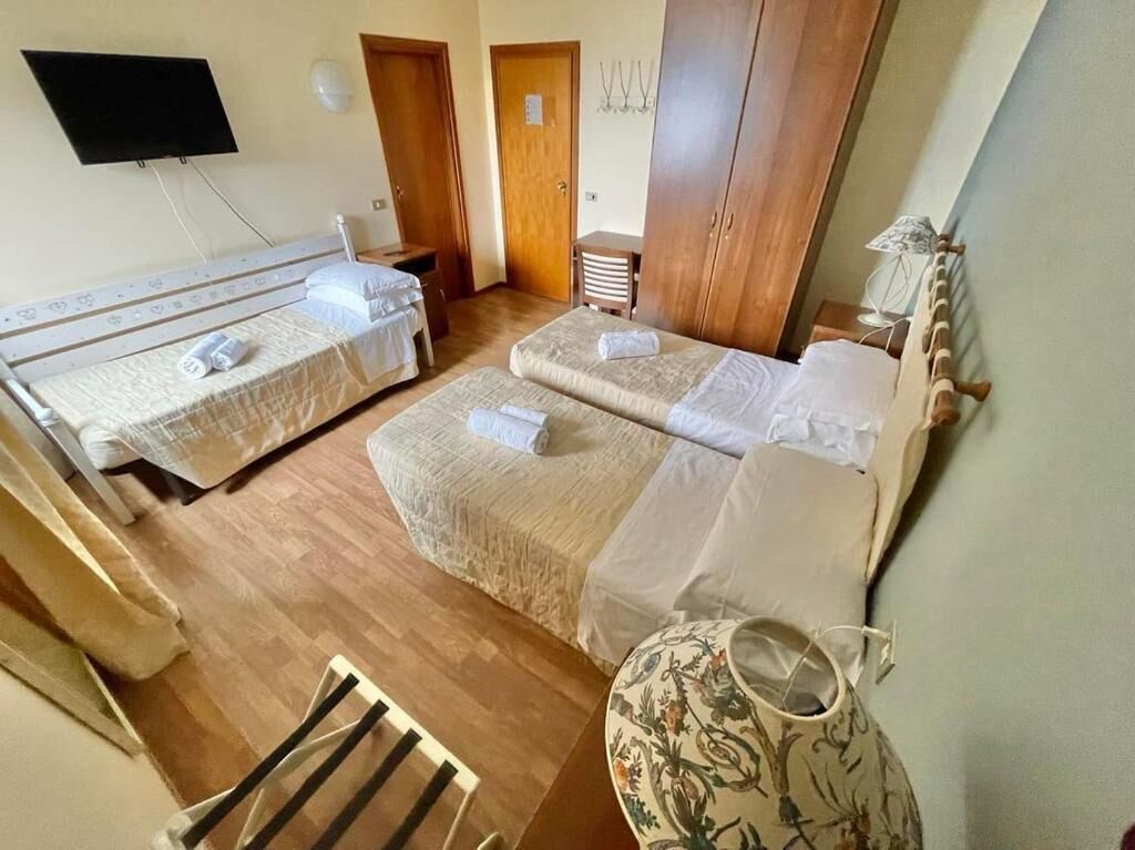 Ein Hotelzimmer mit zwei Betten, einem Fernseher, einem Holzschrank und einer Ziervase.