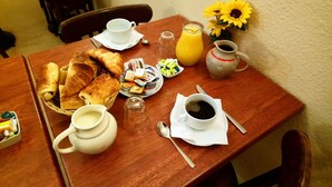 Een ontbijttafel met croissants, koffie, sap en een vaas met zonnebloemen.
