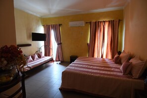 A hotel room with a bed, a sofa bed, a TV, and a window with curtains. - Hôtel de la Poste (Saint-Claude)
