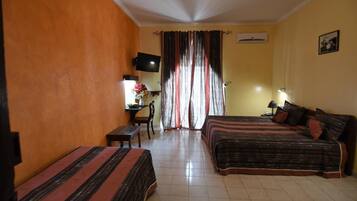 A hotel room with two beds, a desk with a chair, a TV, and a window with curtains.