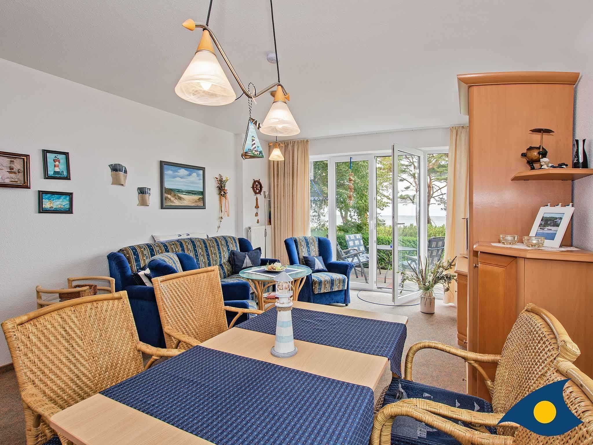 Un salon chaleureux avec un canapé, des fauteuils, une table à manger et une vue à travers une porte vitrée.