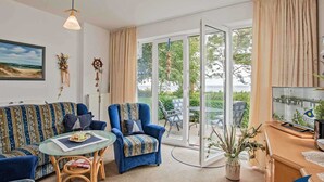 A living room with a sofa, armchairs, a glass coffee table, and a TV. - Villa Strandperle, Whg. 22 - VS 22 (Heringsdorf)