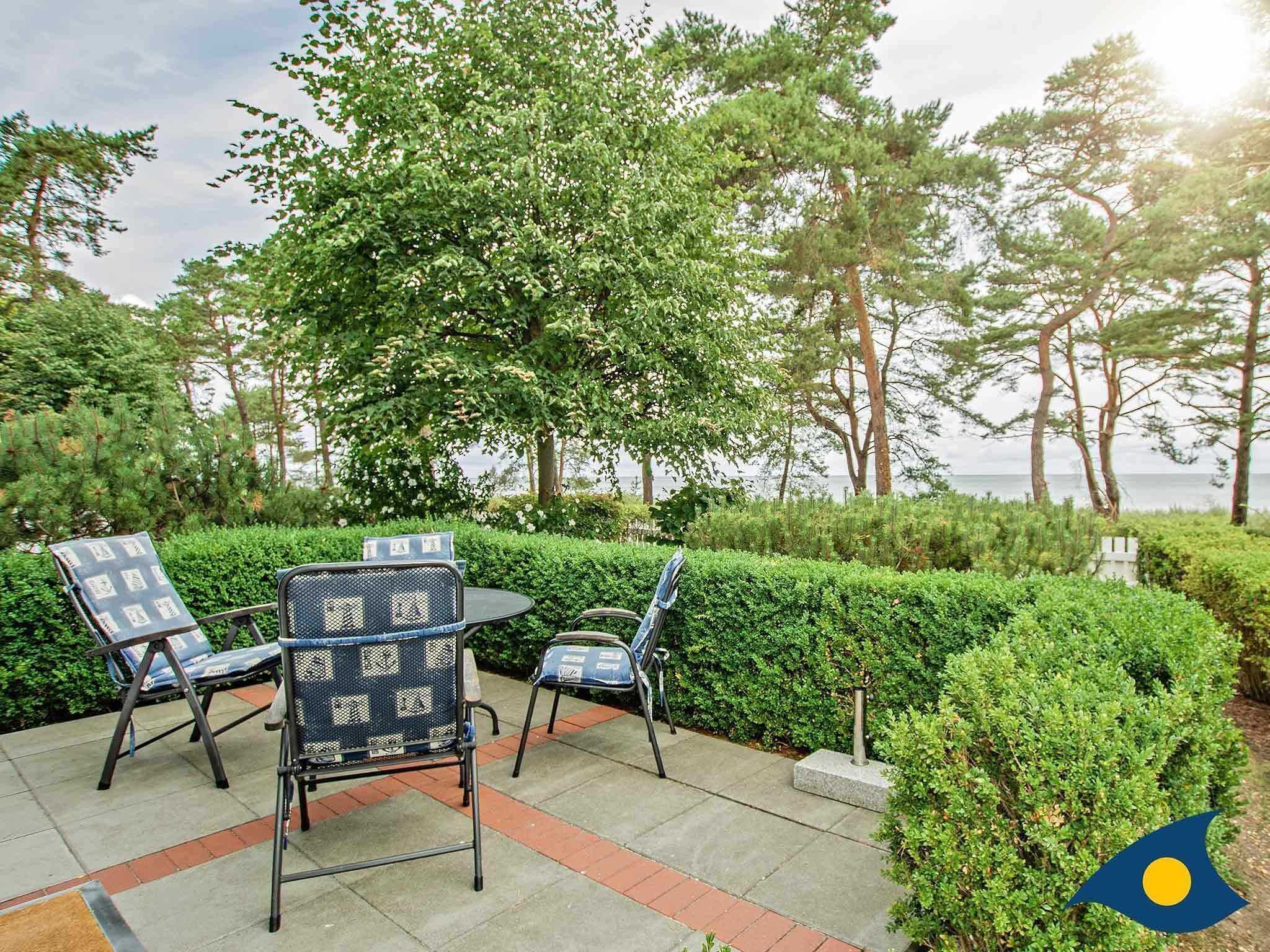Un espace extérieur aménagé avec des chaises et une table, entouré de verdure et d’arbres, et offrant une vue sur une étendue d’eau.