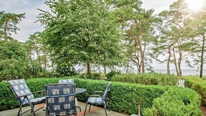 An outdoor seating area with chairs and a table, surrounded by greenery and trees, overlooking a body of water. - Villa Strandperle, Whg. 22 - VS 22 (Heringsdorf)