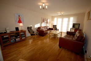A living room with a brown leather sofa, a wooden coffee table, a bookshelf, and a television on a stand. - Welcoming, spacious, accessible, City Centre apt, with parking and wifi. (Edinburgh)