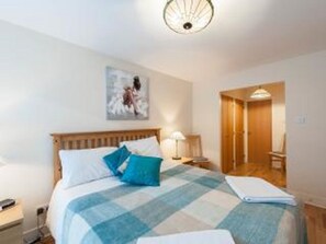 A neatly made bed with a blue and white checkered blanket, a bedside lamp, and a painting on the wall. - Welcoming, spacious, accessible, City Centre apt, with parking and wifi. (Edinburgh)