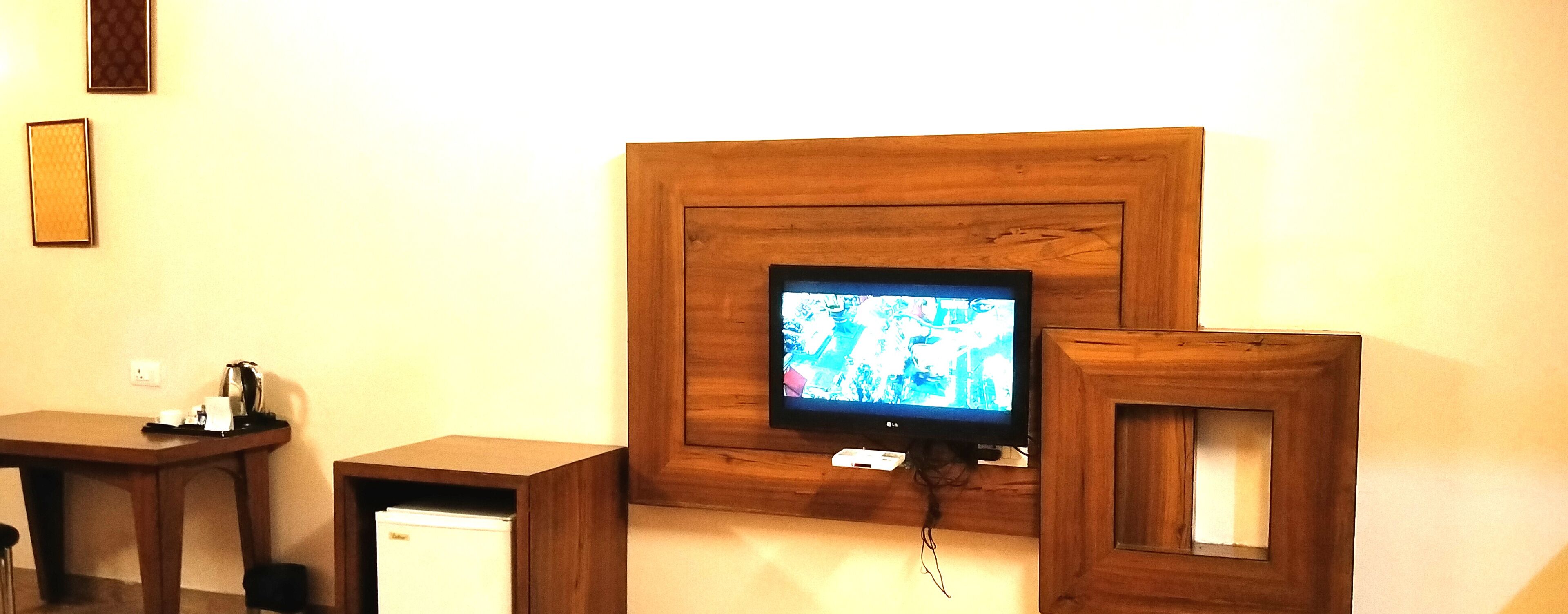 A television mounted on a wooden wall with a small table and a refrigerator below it.