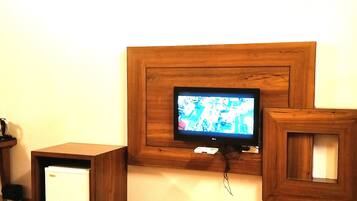 A television mounted on a wooden wall with a small table and a refrigerator below it.