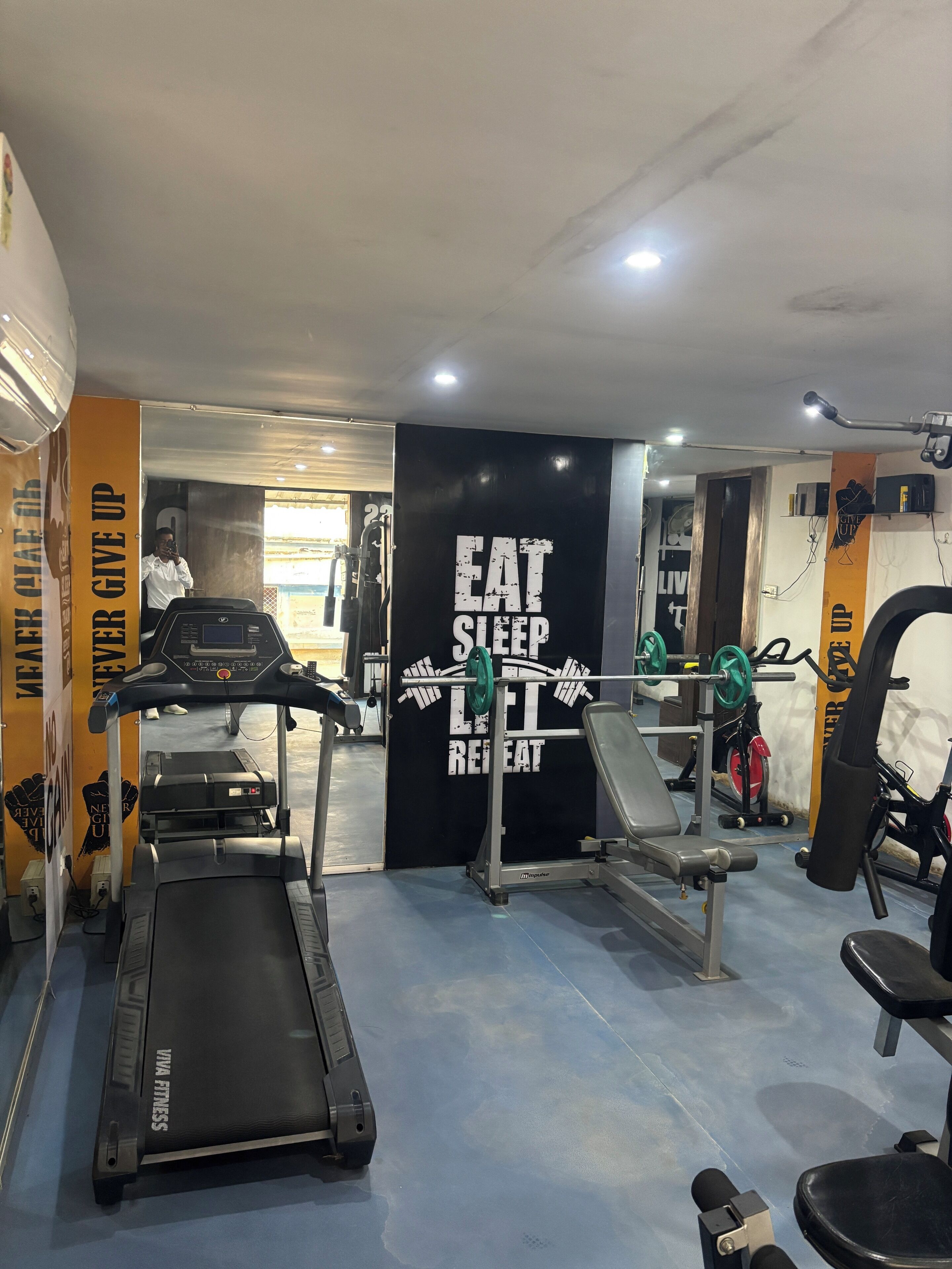 Une salle de sport équipée de tapis de course, d’un banc de musculation et d’une affiche motivante.