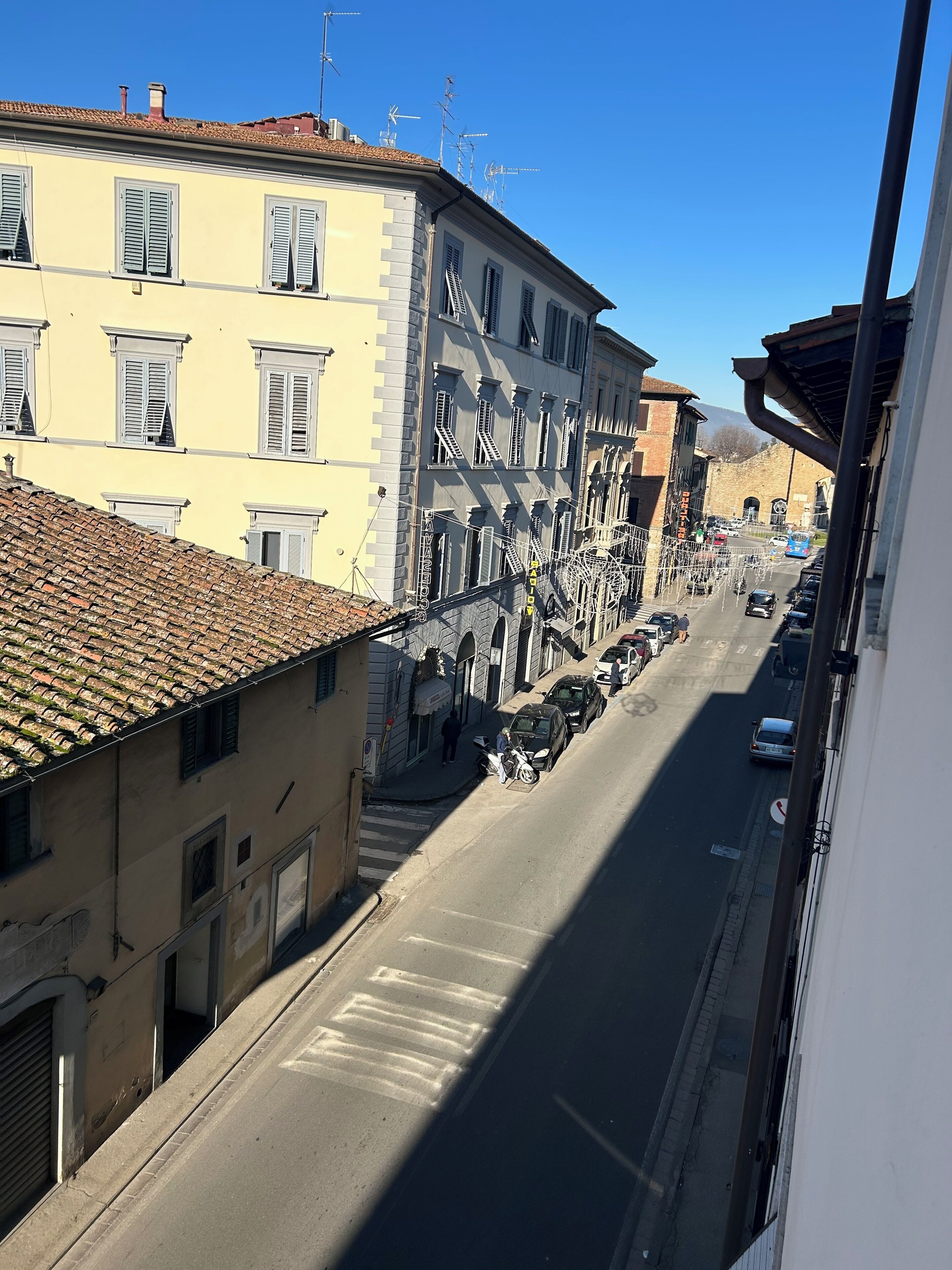 A street view with buildings, a clear sky, and a few parked cars.