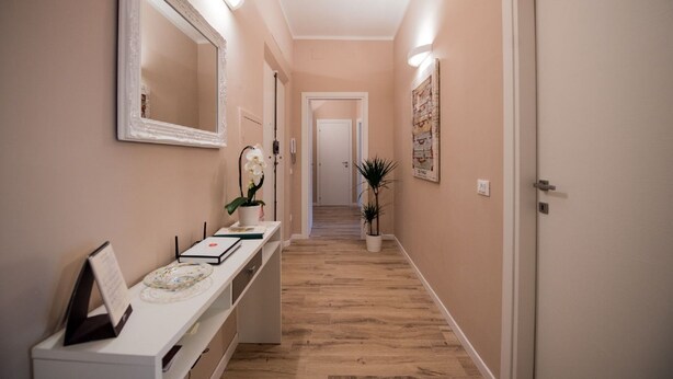 A hallway with a reception desk, a large mirror, a potted orchid, a framed picture, and a door at the end.