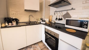 A modern kitchen with white cabinets, a black countertop, a stainless steel sink, a black range hood, a microwave, and a built-in oven.