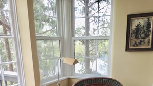 A room with a wicker chair, a small round table with a plant, and a floor lamp.