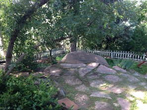 Ein Garten mit Holzzaun, großen Steinen und verschiedenen Pflanzen.