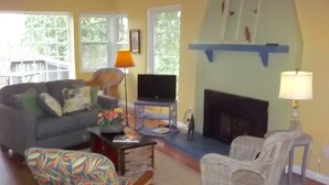 A living room with a sofa, chairs, a television, a fireplace, and a window with a view of trees.